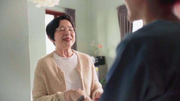 高级亚洲妇女欢迎亚洲女护士穿着工作服家庭护工访问在入口处微笑和一点交谈家庭健康护理和养老院