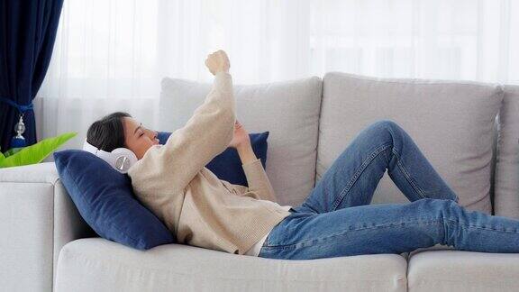 快乐的年轻亚洲女性在家里放松女人笑着躺在沙发上跳舞听音乐