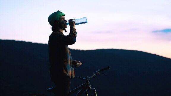 骑山地车的年轻人在日落时喝水