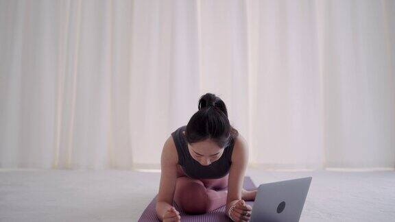 年轻的亚洲女性看着笔记本电脑在室内练习瑜伽