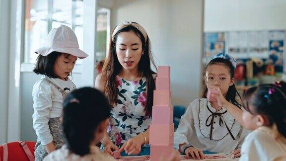 亚裔华裔蒙氏幼教老师在教室里向学生展示用玩具积木搭塔