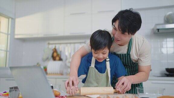 爸爸和可爱的小儿子正在做饼干通过社交媒体上的视频在平板电脑上一起在厨房做饭玩得很开心烹饪概念和家庭时代