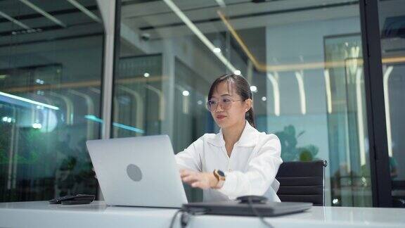 使用笔记本电脑的亚洲女性在工作结束后伸展一下身体在办公室关闭或关闭笔记本电脑劳累过度的工人结束工作休息放松