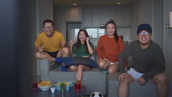 4K一群亚洲人朋友在家里一起看电视上的竞技体育比赛