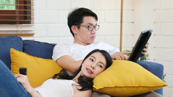 年轻的亚洲夫妇看电视与幸福在家庭客厅的沙发背景人和家庭娱乐