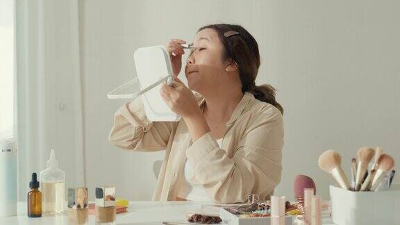 年轻的亚洲女子在家里的卧室里用睫毛膏涂睫毛