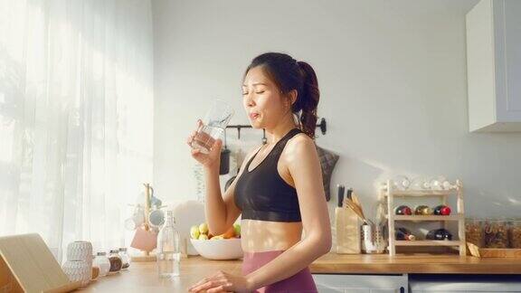 穿着运动服的亚洲美女运动后在家喝水年轻的口渴活跃的运动女孩喝干净的天然矿物在杯子锻炼后在家里的厨房保健