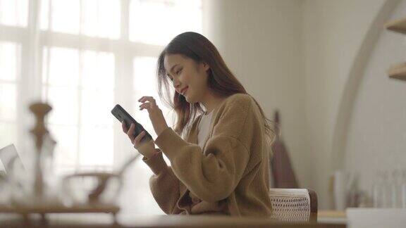 快乐的年轻亚洲女人在家里放松亚洲女性站在厨房柜台使用手机