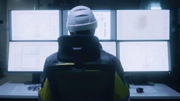 工业4.0现代工厂:设施操作员戴安全帽和安全背心控制车间生产线使用电脑和屏幕显示机械控制操作界面后视图放大