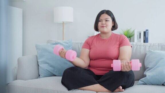 亚洲年轻的大码女孩使用哑铃锻炼在客厅在家里有吸引力的特大号身材的女孩遵循电视上的在线教练的健身指导视频在家里减肥