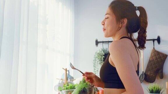 亚洲吸引人的运动女子拿着沙拉碗吃蔬菜美丽的运动女孩在运动服享受吃干净的蔬菜锻炼后的健康在家里饮食与健康食品理念