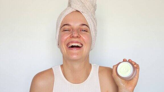 清洁清爽的皮肤护理水疗恢复活力面部健康护理微笑的满意的女人在她的脸上涂抹面霜或保湿霜孤立在白色的背景上
