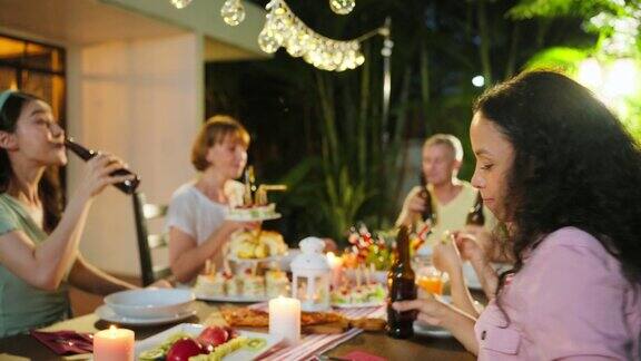 多民族大家庭在户外的花园中欢聚迷人的各色人聚在餐桌前共进晚餐吃着美食庆祝周末团圆