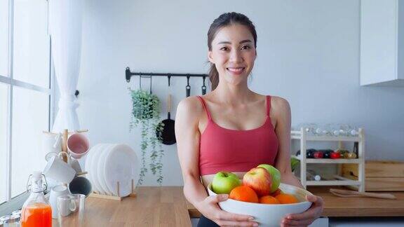 亚洲美女肖像拿着水果盘看着相机漂亮的运动女孩穿着运动服在家里享受运动后吃干净的蔬菜的健康饮食和健康食品
