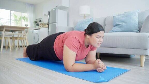 亚洲年轻的加码女孩试图坐起来锻炼在客厅有吸引力的特大号身材女孩为健康保健和使用垫子锻炼减肥遵循在线指导在家里
