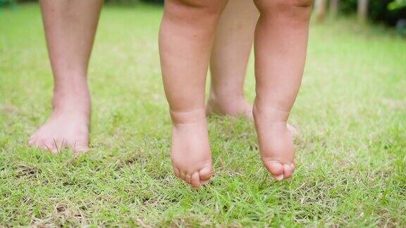 快乐可爱可爱的小亚洲女婴在爸爸的帮助下学会了第一步走路赤脚在新鲜的绿色草地上健康的生活方式儿童发展家庭和育儿