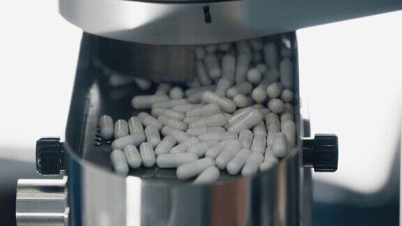 4K白色胶囊从金属传送带上落下现代化制药厂的自动生产线工作过程中药品在传送带上的运动特写景深