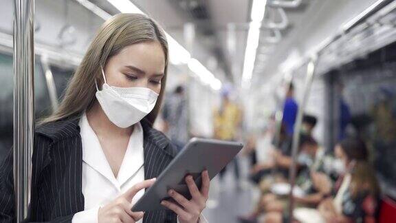 戴着防护口罩的女商人在地铁上使用电子平板电脑