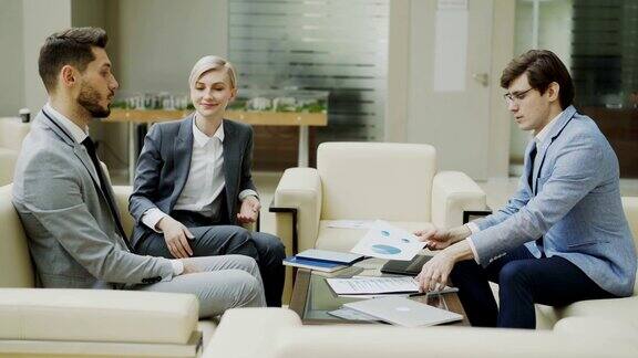 镜头拍摄的商人与男女商业伙伴坐在现代办公大厅的沙发上讨论财务报告
