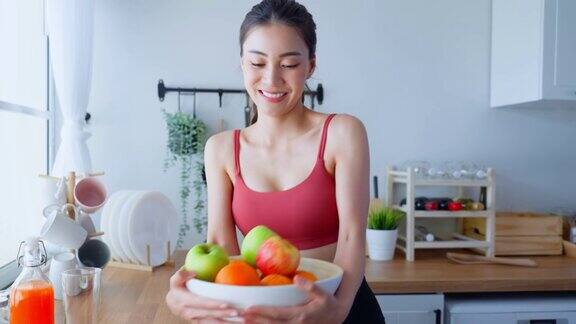 亚洲美女肖像拿着水果盘看着相机漂亮的运动女孩穿着运动服在家里享受运动后吃干净的蔬菜的健康饮食和健康食品