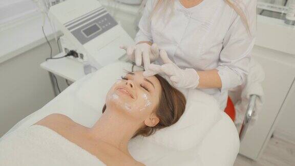 女美容师按摩时在脸上涂抹面霜美容临床护理、放松、年轻化、滋养面部肌肤、抚平皱纹一个女孩在美容院做水疗