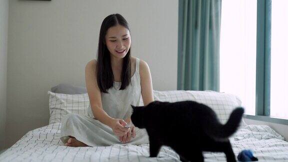 4K年轻的亚洲妇女在卧室的床上喂她的黑猫