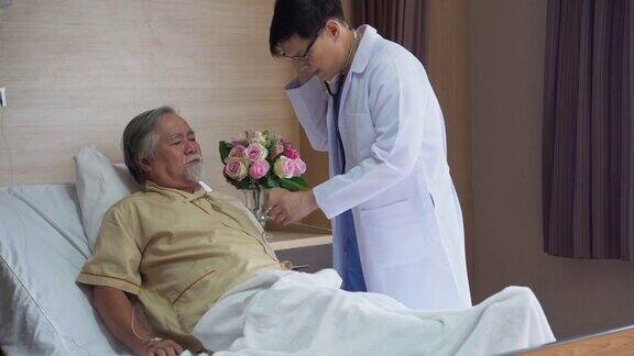 一位亚洲老年患者在床上咳嗽年轻的医生用听诊器在医院检查心肺