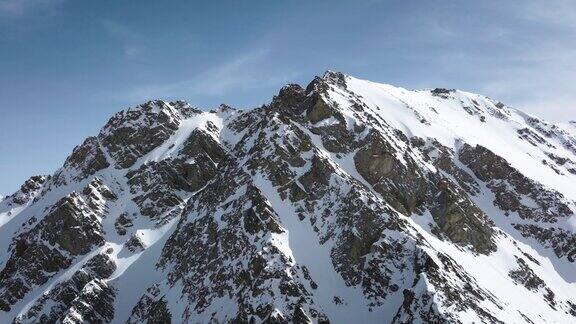 鸟瞰图在欧洲阿尔卑斯山的岩石山峰之间飞行冬天被雪覆盖自然视频背景