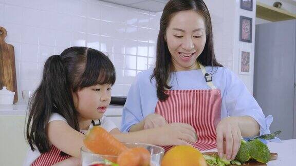 亚洲母女穿着围裙在厨房里妈妈正在教她的女儿在做饭前如何准备水果和蔬菜