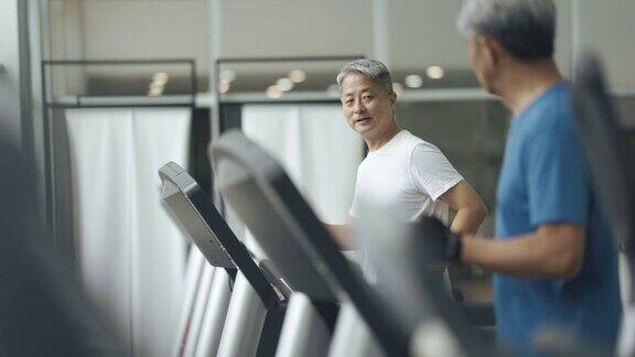 两名中国老人一起在健身房的跑步机上跑步