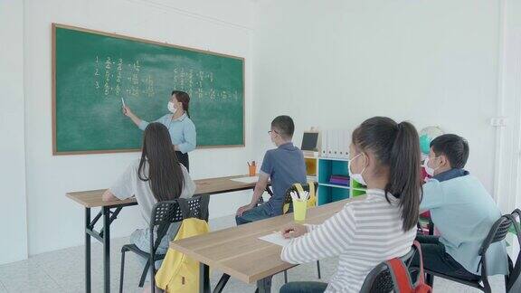 一群亚洲小学生和教师戴着卫生口罩在教室里防止Covid-19的爆发返校时重新开学教育理念的新常态