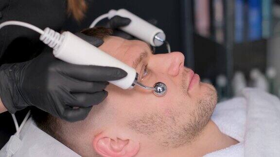 一位美容师用电动振动器给一位有魅力的年轻人做面部按摩