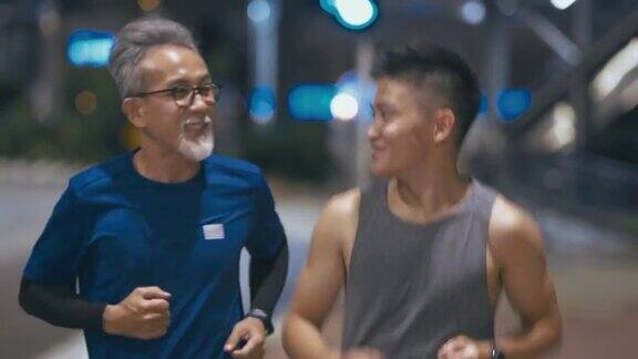 亚洲华人活跃的老人和儿子晚上下班后一起在城里跑步慢跑