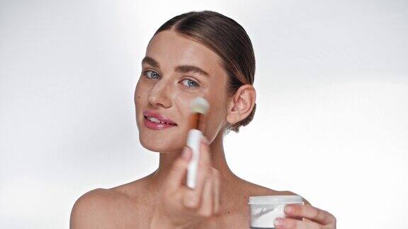 年轻的成年女性用化妆刷在白色的脸上涂高光