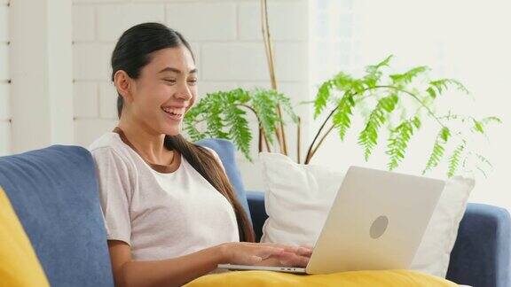年轻美丽的亚洲女人与笔记本电脑工作坐在家里客厅的沙发上人与科技在家里工作在线教育