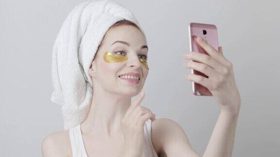 戴着金色眼罩和毛巾的女士用手机自拍或视频通话