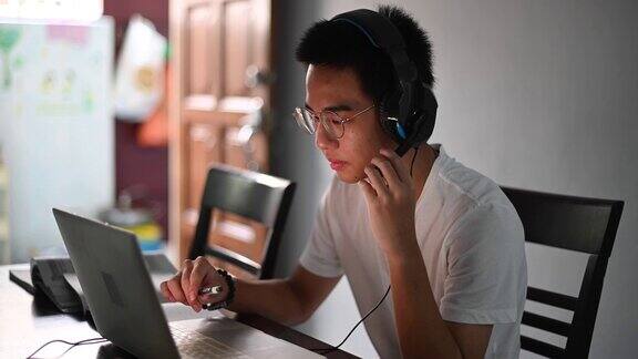 一名亚裔中国少年一边在厨房餐桌上做作业一边通过网络软件与所有同学在线聊天
