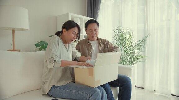 快乐的亚洲夫妇坐在家里客厅的沙发上开心地接收和打开纸箱生活方式花时间在家里