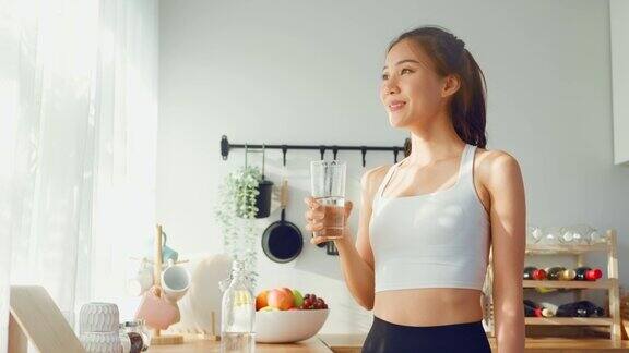 亚洲美女穿着运动服在家运动后喝水年轻的口渴活跃的运动女孩喝干净的矿物自然在杯子锻炼后保健在厨房在房子