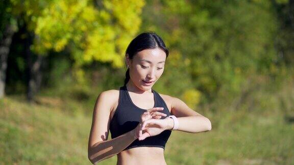 运动亚洲女性看智能手表在现代田径运动员使用使用智能手表健身手环画像
