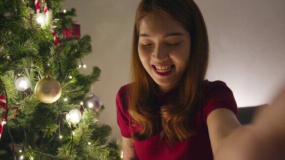 年轻的亚洲女性用智能手机视频通话与夫妇圣诞礼物盒圣诞树装饰在家里客厅