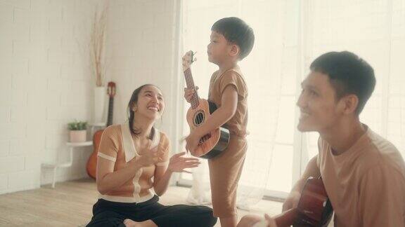 通过音乐建立快乐的亚洲家庭:父母和儿子在家里弹吉他