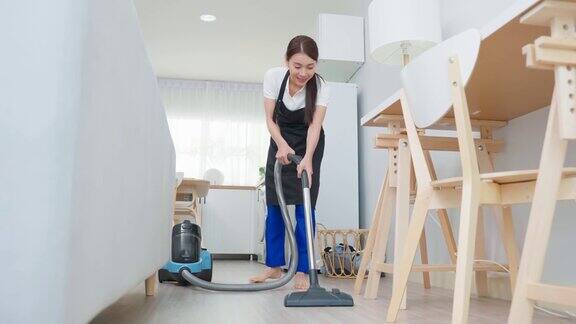 亚洲清洁服务女工清洁客厅在家里美丽的年轻女孩管家清洁工穿围裙和吸尘肮脏的地板家务和家务在房子