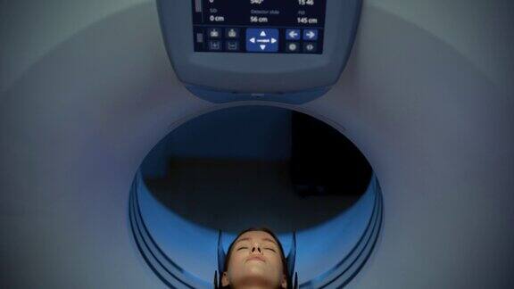 摄像机从控制屏幕平移到患者:医学实验室或医疗机构使用高科技设备对躺在CT或MRI上的女性进行扫描同时机器扫描她的大脑