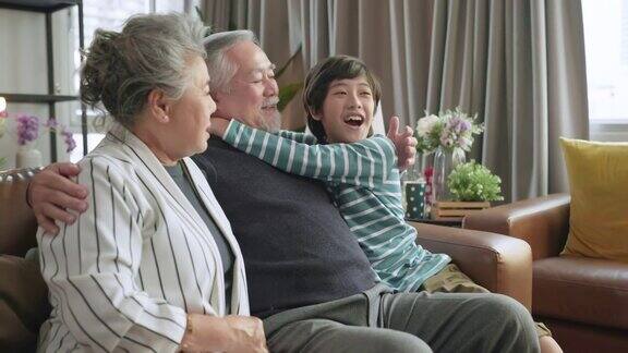 快乐的亚洲家庭爱成熟的祖父母坐在客厅的沙发上休息和小孙子享受周末微笑的亚洲老年祖父母放松在家里的沙发上和可爱的孙子聊天