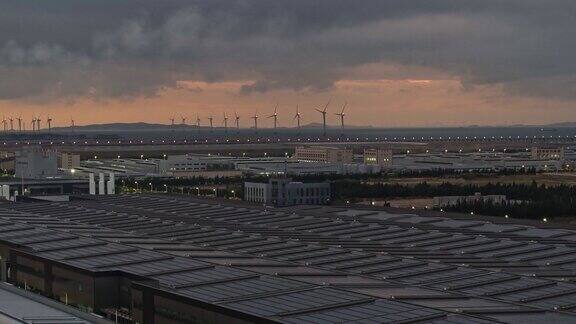 日出前的工厂屋顶太阳能发电厂和远处的风力涡轮机