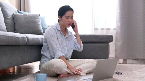 一位年轻的亚洲女商人正在家里的客厅里用笔记本电脑工作她接到了上司的电话在家工作商业女性和工作理念