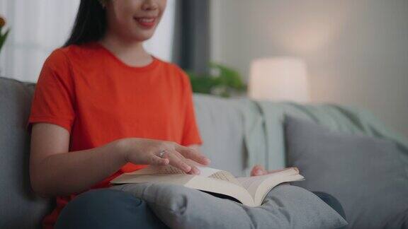 年轻的亚洲女子坐在客厅的沙发上看书