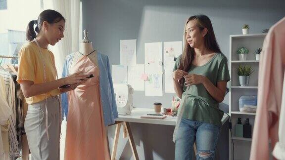 两位专业的亚洲快乐女士时装设计师与休闲团队合作用数码平板测量带在假人上创造服装设计女裁缝生意伙伴与创业