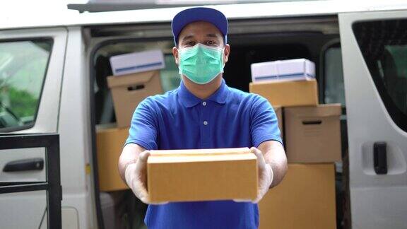 冠状病毒概念蓝色快递英俊的亚洲男子拿着包裹纸盒与防护口罩和医用橡胶手套站在货车前面4k分辨率和慢动作拍摄